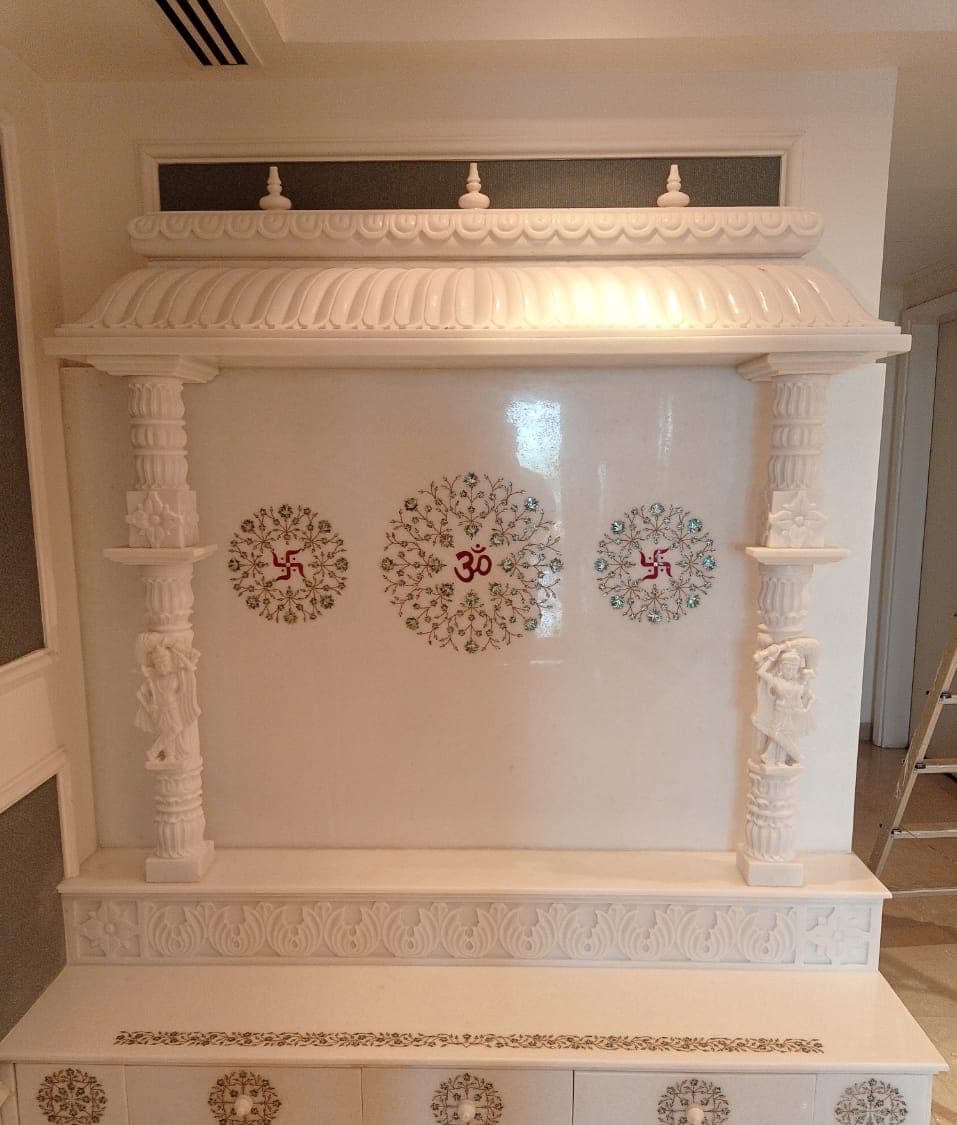 Design inspiration: wide white marble mandir with carved figure pillars, Om inlay and drawer base
