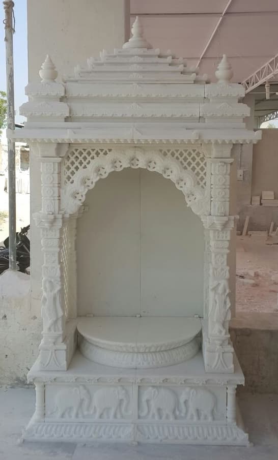 Tall marble mandir with tiered shikhar, jali arch, carved figures and elephant base